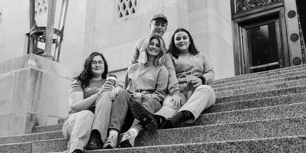 Black and white image of four people sitting on steps outside of a classic courthouse. Easy person is holding a cup of coffee from Rhino Coffee in Shreveport, Louisiana.