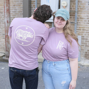 Two people in purple shirts: a white male-presenting with back to camera and a white female-presenting facing camera. Shirts have Rhino Coffee logo and monogram